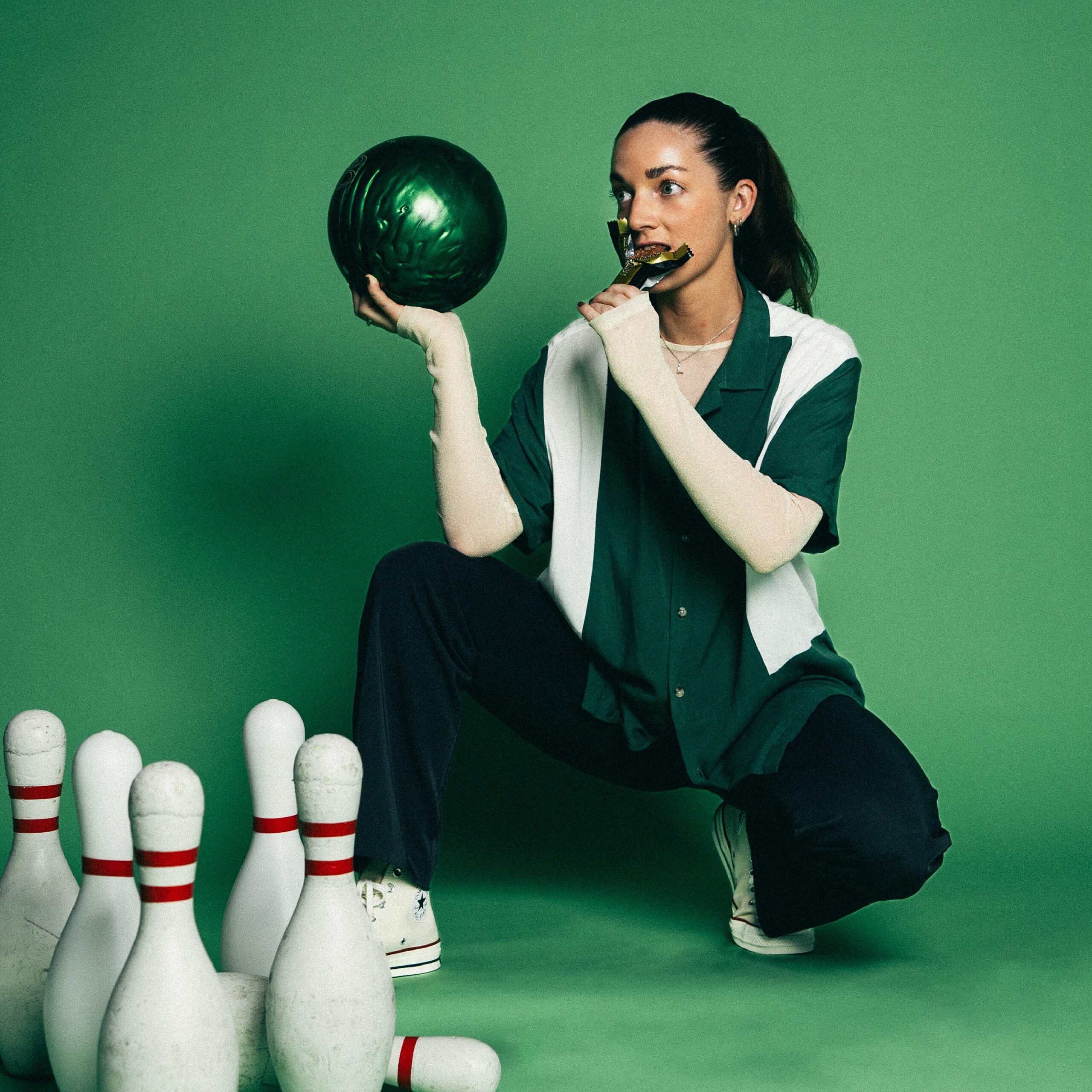 Woman in bowling pose with ball and trophy, surrounded by pins on green background.